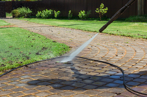 Cleaning street with high pressure power washer, washing stone garden paths.